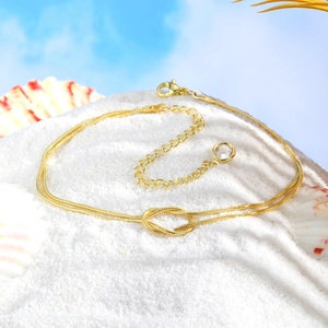Close-up of golden double-strand snake chain anklet with knot design on white beach sand