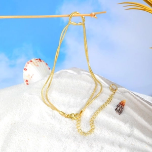 Detail of golden double-layer snake chain anklet with lobster clasp on beach background