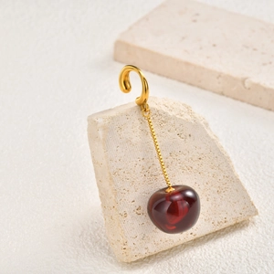 Macro shot of gold cherry clip-on earring hanging on a textured minimalist stone
