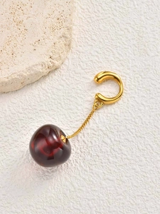 Detail of creative cherry ear cuff with gold chain and deep red resin pendant on stone