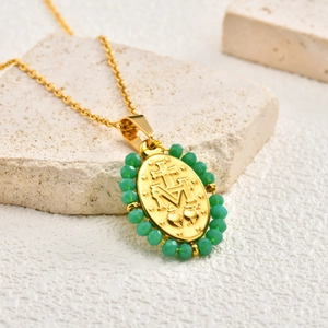 Close-up of gold oval Virgin Mary pendant with green beads on stone background