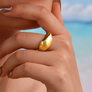 Polished 18K gold teardrop ring with organic curves on a model with a beach background