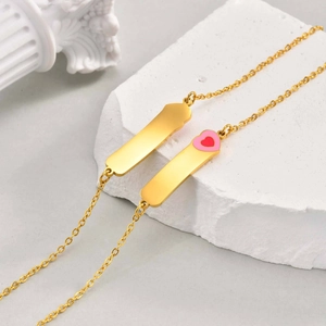 Détail de gourmettes en acier doré avec un charm en forme de cœur en émail rose