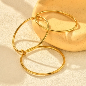 Macro shot of three stacked polished gold hoop earrings on a textured ceramic surface