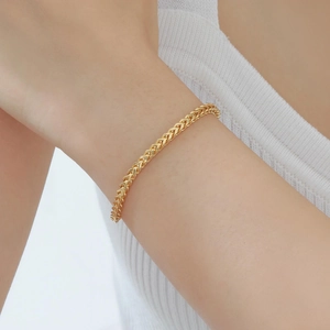 Detail of elegant gold wheat link chain bracelet on a model wrist against white knitwear