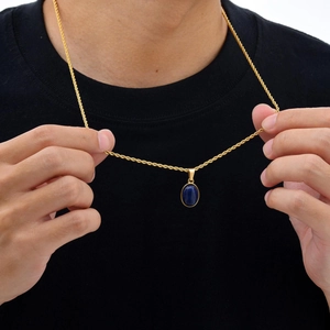 Detail van een gouden gedraaide ketting met ovale blauwe steen hanger bij een model