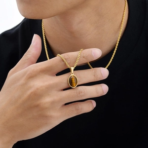 Detailopname van gouden koordketting met ovale tijgeroog hanger gedragen op een zwart shirt