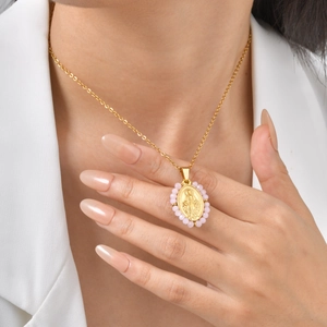 Detail of gold necklace with oval Virgin Mary pendant and light pink beads on a model