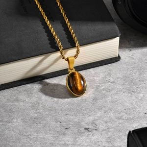 Detail van een gouden touwketting met een ovale tijgeroog steen hanger in vintage stijl