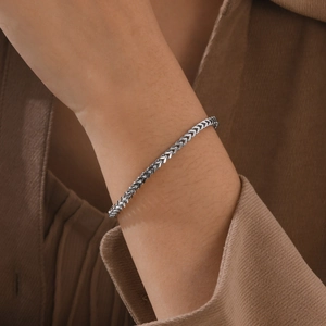Close-up of a silver wheat chain bracelet on a wrist with brown corduroy attire