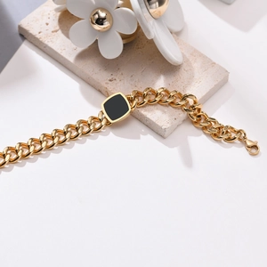 Detail of gold Cuban chain bracelet with black square element and lobster clasp