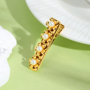 Detailed view of golden flower hair clip with pearls on a decorative ceramic plate