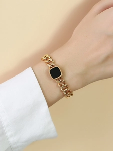 Detail of a golden square pendant bracelet with black enamel inlay on a woman's wrist