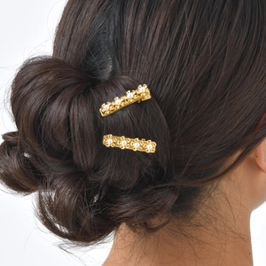 Detailed view of two gold flower hair clips with pearls worn by a model in hair