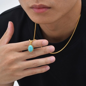 Detailopname van een gouden ketting met ovale turkooizen hanger gedragen door een man