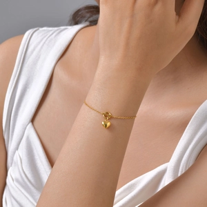 Détail d'un bracelet doré 18K avec pendentif cœur et fermoir à bascule sur le poignet