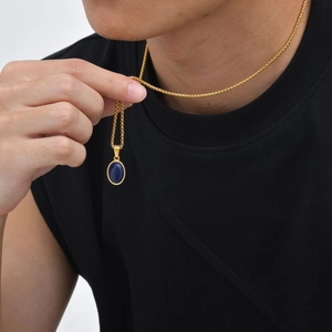 Macro-opname van gouden ketting en blauwe ovale lapis lazuli hanger op zwart shirt