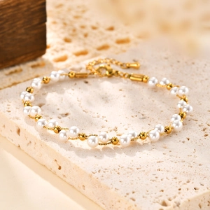 Gros plan d'un bracelet de perles et billes dorées avec fermoir mousqueton et breloque