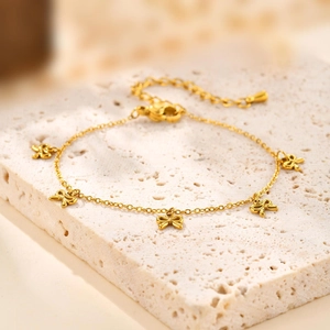 Détail du bracelet chaîne doré avec cinq pendentifs nœuds sur une surface en pierre beige