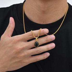 Detailopname van een ovale zwarte stenen hanger aan een gouden boxketting bij een persoon