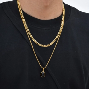 Detail van gelaagde gouden schakelkettingen met een ovale zwarte stenen hanger