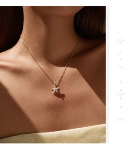 Detail of silver starfish necklace with white pearls worn by model under artistic lighting