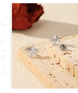 Macro shot of silver starfish earrings with inlaid pearls on a textured stone surface