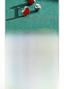 Detail of red enamel heart stud earrings with silver screw-back closure on green background