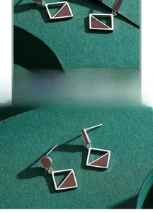 Macro detail of geometric silver earrings with brown enamel on dark green textured paper