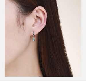 Close-up of model wearing s925 silver drop earrings with rectangular green gemstones