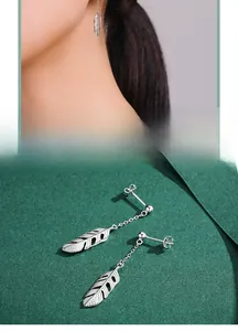 Detailed view of S925 silver feather drop earrings with thin chains on a green texture