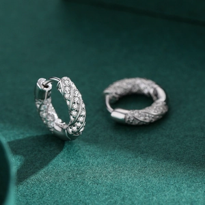 Pave setting cubic zirconia twisted silver hoop earrings for women on dark green surface