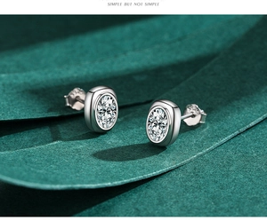 Macro shot of S925 sterling silver oval zircon studs showing the S925 hallmark on a green background