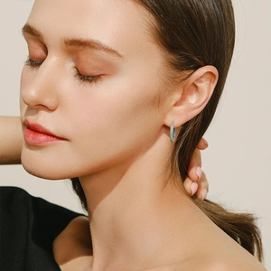 Sterling silver hoop earrings with turquoise stones worn by model on beige background