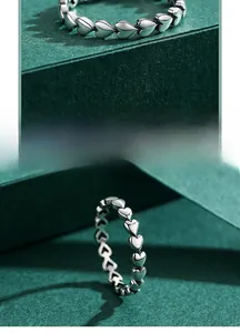 Detailed view of silver heart-shaped woven ring design on elegant dark green display