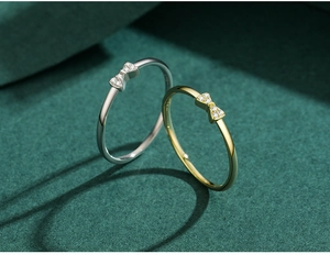 Close-up of gold and silver bow rings with micro-pave zircons on a dark green background