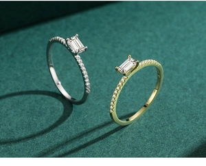 Macro detail of silver and gold emerald cut zircon rings with pave setting on green base