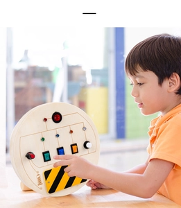 Close-up of a child interacting with the wooden busy board featuring colorful LED switches