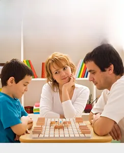 Family playing strategy board game with wooden grid base and colorful peg figures