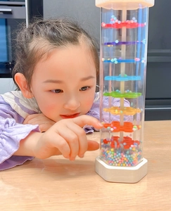 Asian child playing with colorful rainmaker toy showing internal beads and rotators
