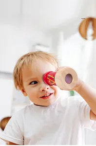 Close-up of a child using a red kaleidoscope educational toy in a bright home setting