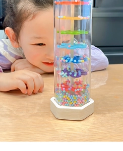 Close-up of rainbow rainmaker toy with colorful beads and rotating blades for baby sensory play