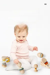 Toddler playing with natural wooden rattle set featuring pastel eco-friendly paint