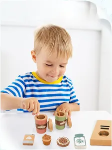 Bambino gioca con set da caffè in legno con tazze, biscotti e cartone del latte