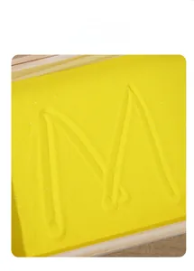 Vue macro de sable fin jaune dans un plateau en bois montrant la lettre M pour tracer