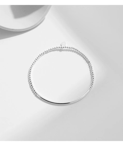 Dettaglio del bracciale con perle d'argento, tubo curvo e ciondolo a cuore su grigio chiaro