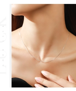 Detalle macro de una cadena de plata minimalista en el cuello con texto Good Luck