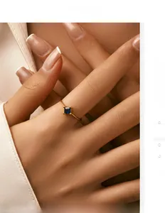 Close-up of a slim gold ring featuring a minimalist square blue gemstone on finger