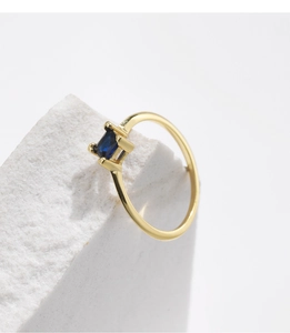 Close-up of a square-cut blue sapphire set in a thin gold band on a white stone background