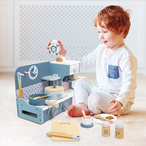 Wooden play kitchen set with blue stovetop and pans used by a boy in a cozy room